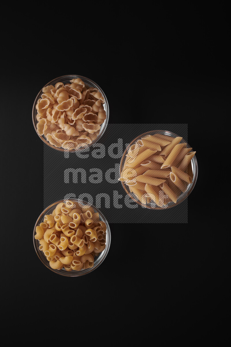 Different pasta types in glass bowls on black background