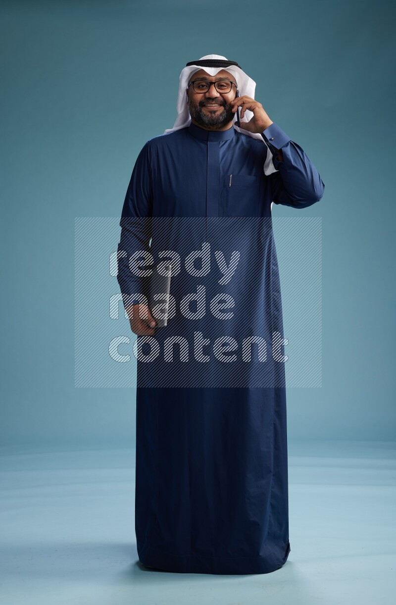 Saudi Man with shimag Standing talking on phone on blue background