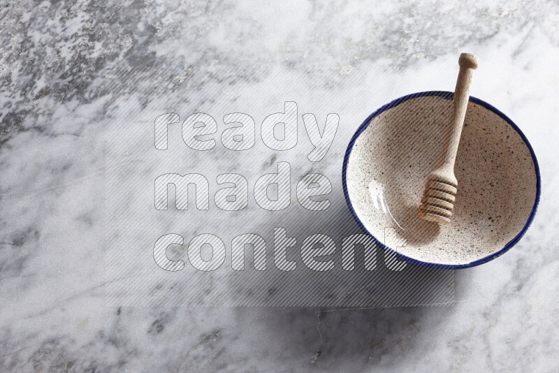 Multicolored pottery bowl with wooden honey dipper in it on grey marble background