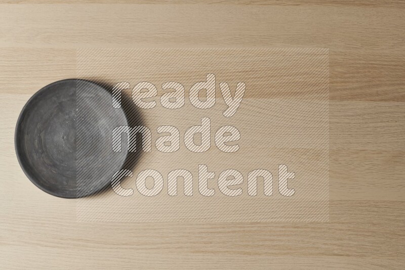 A circular black pottery plate on light wooden background