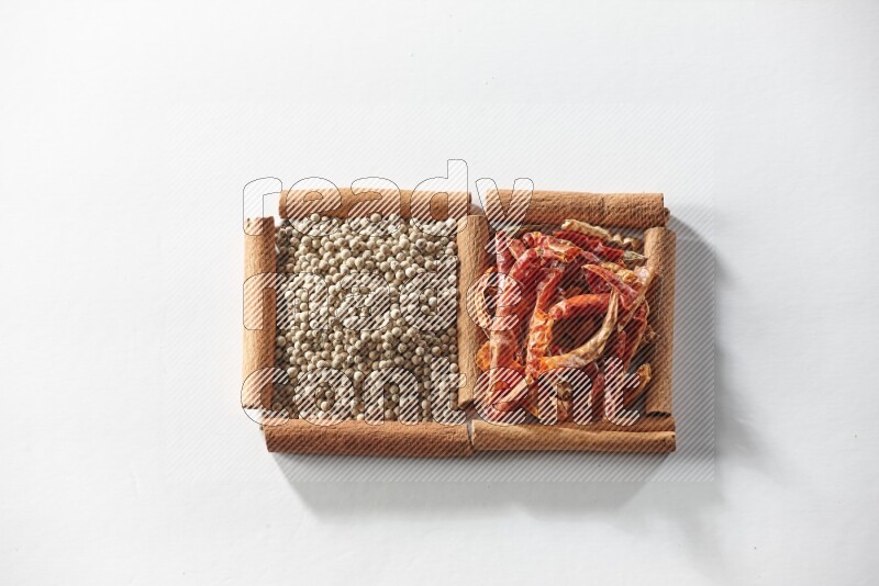 مربعان من أعواد القرفة ممتلئان بالفلفل الحار المجفف وحبوب الفلفل الأبيض علي خلفية بيضاء