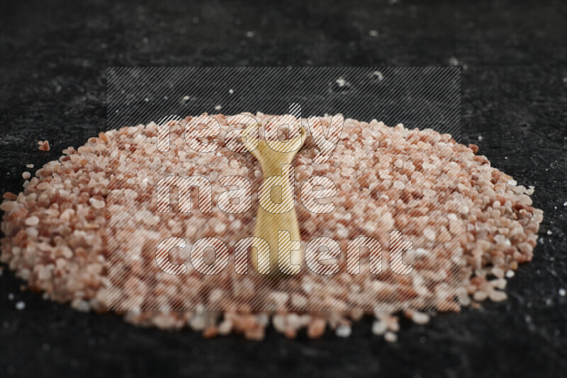 ملعقة خشبية ممتلئة ببلورات ملح الهيمالايا الخشنة على حفنة من الملح على خلفية سوداء