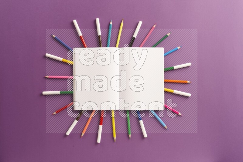 A blank open notebook with school supplies on purple background