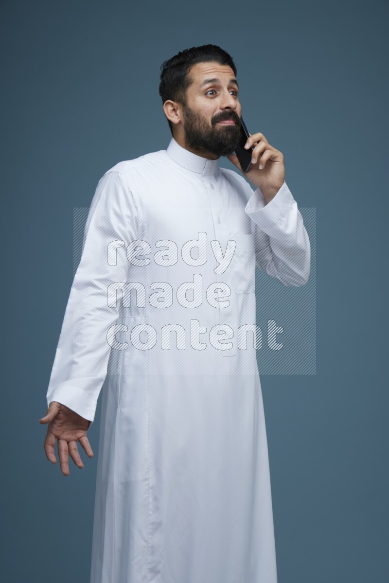 A man having a call on a blue background wearing Saudi Thob