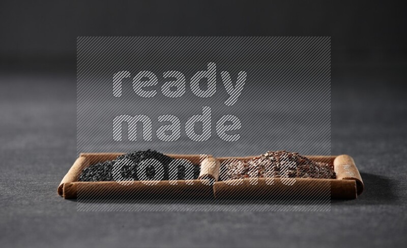 مربعان من أعواد القرفة ممتلئان ببذور الكتان وحبة البركة السوداء علي خلفية سوداء