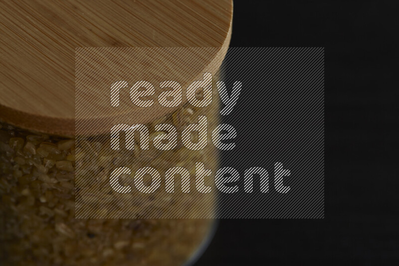 Coarse bulgur in a glass jar on black background