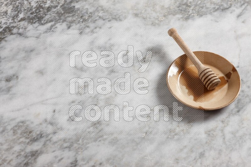 Multicolored pottery plate with wooden honey dipper in it on grey marble background