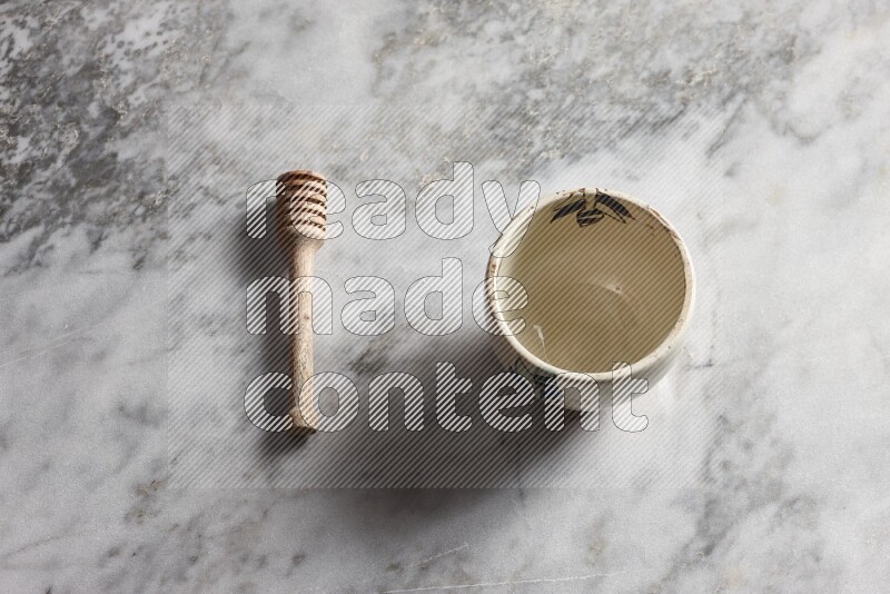 Decorative pottery bowl with wooden honey dipper on the side on grey marble background
