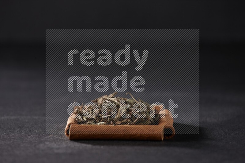 أربعة من أعواد القرفة مكونة شكل مربع بداخلها ريحان مجفف علي خلفية سوداء