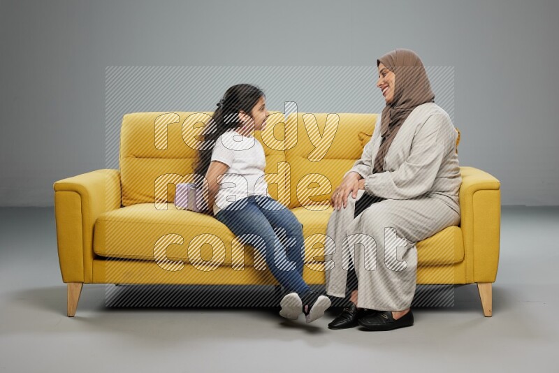 A girl sitting hiding a gift behind her back for her mother on gray background