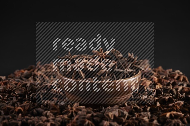 Star Anise in a wooden bowl and surrounded by more anise filling the frame on black flooring