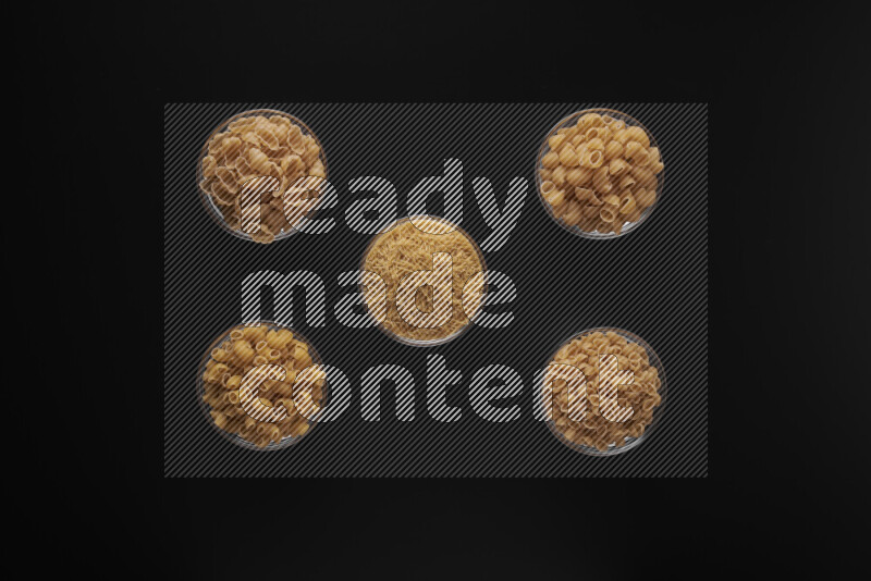 Different pasta types in 5 glass bowls on black background