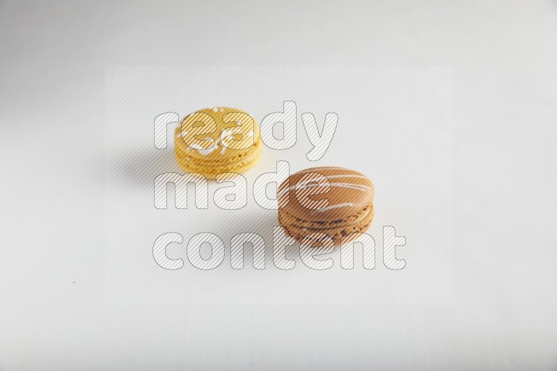 45º Shot of of two assorted Brown Irish Cream, and Yellow Piña Colada macarons on white background