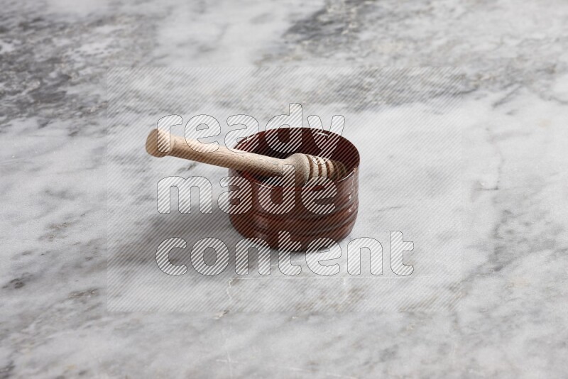 Brown pottery bowl with wooden honey dipper in it on grey marble background