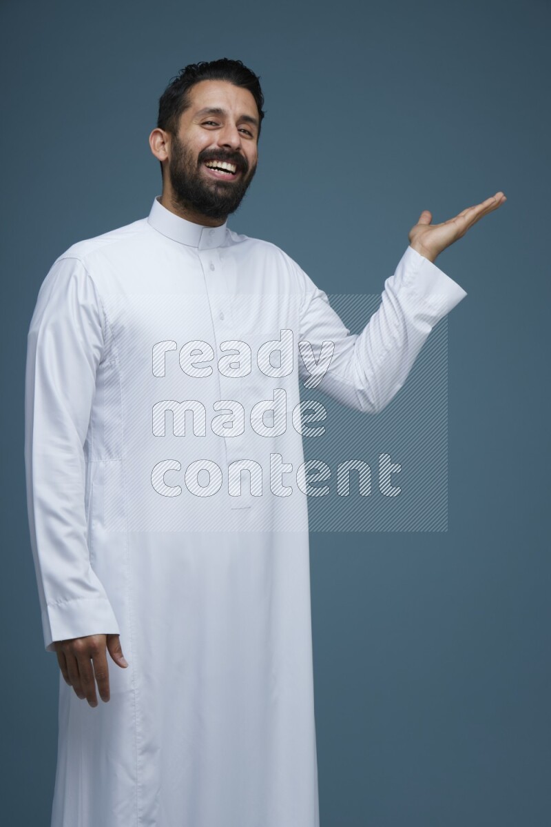 A man pointing in a blue background wearing Saudi Thob