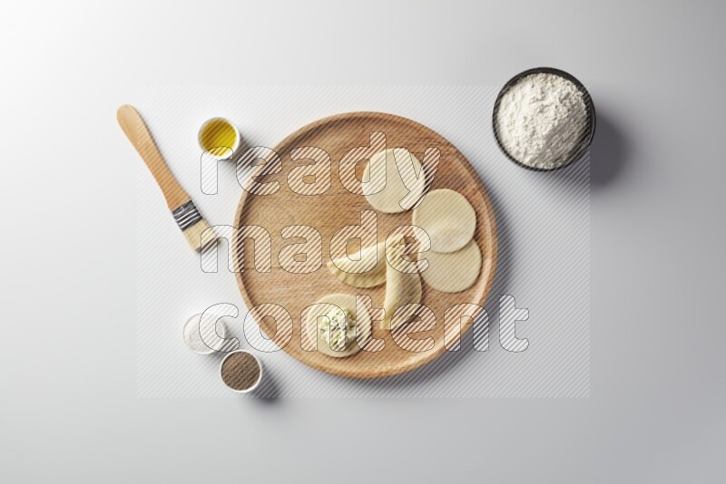 two closed sambosas and one open sambosa filled with cheese while flour, salt, black pepper and oil with oil brush aside in a wooden dish on a white background