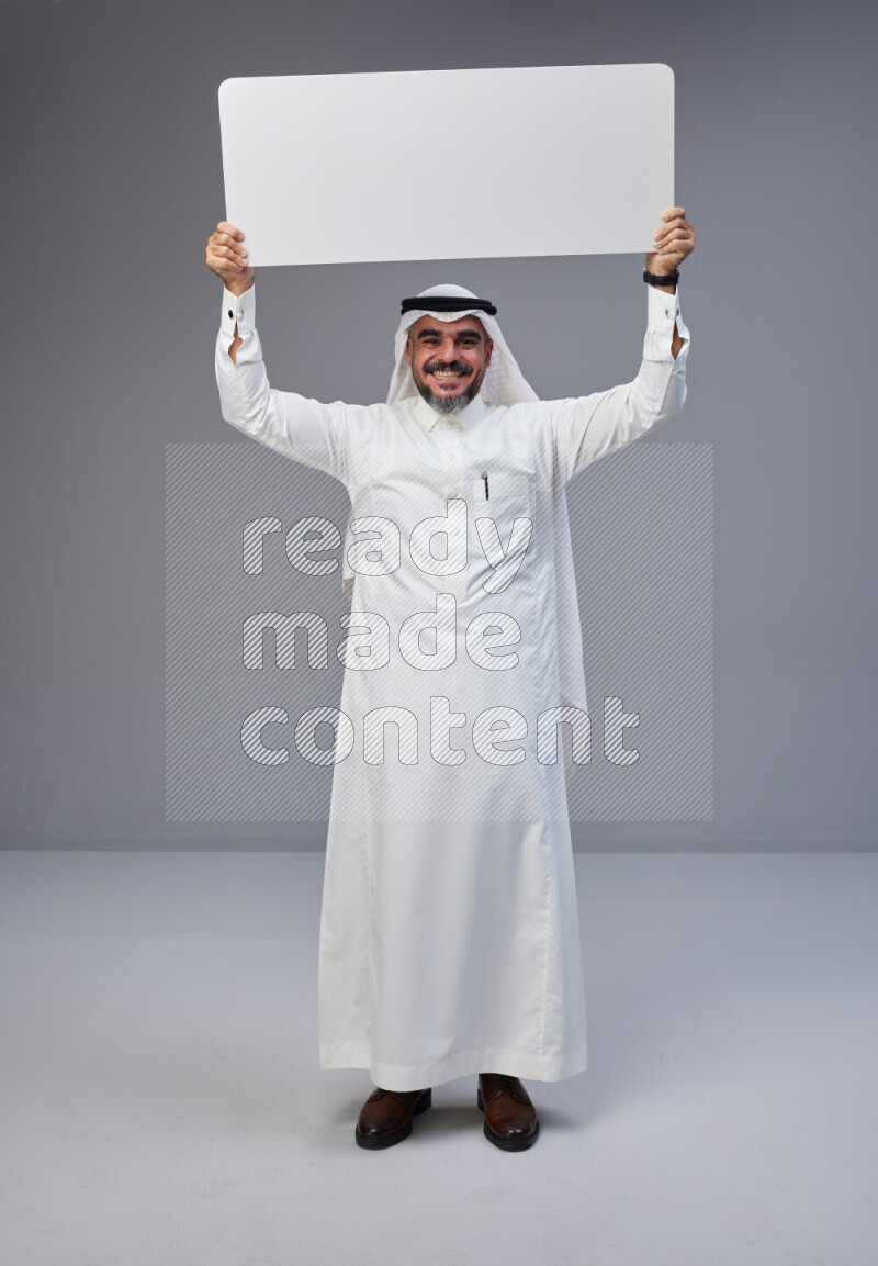 Saudi man Wearing Thob and white Shomag standing holding board on Gray background