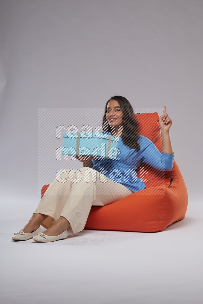 A woman sitting on an orange beanbag and opining a gift