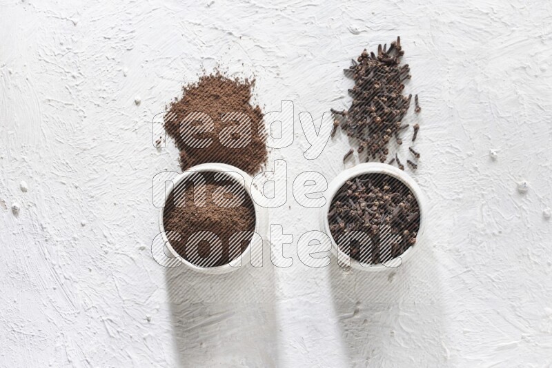2 Beige ceramic bowls, one full of cloves and the other full of powder on textured white flooring