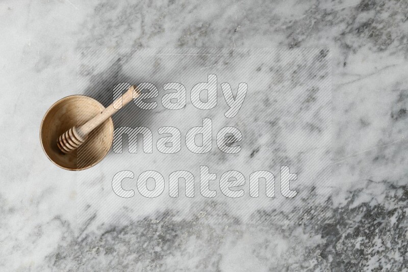 Beige pottery bowl with wooden honey dipper in it on grey marble background