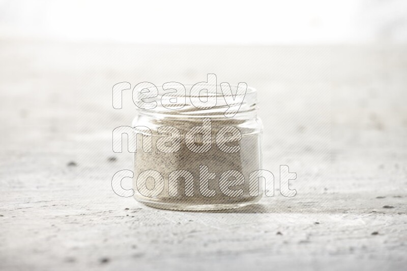 A glass jar full of white pepper powder on textured white flooring