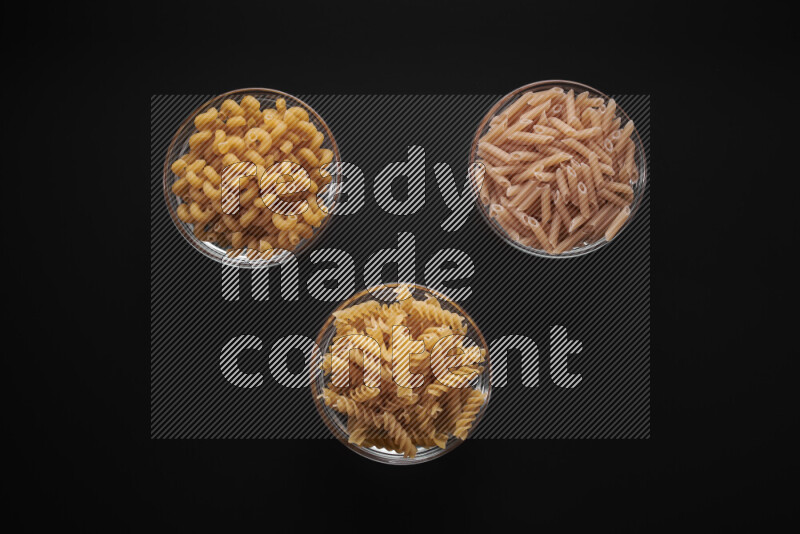 Different pasta types in glass bowls on black background