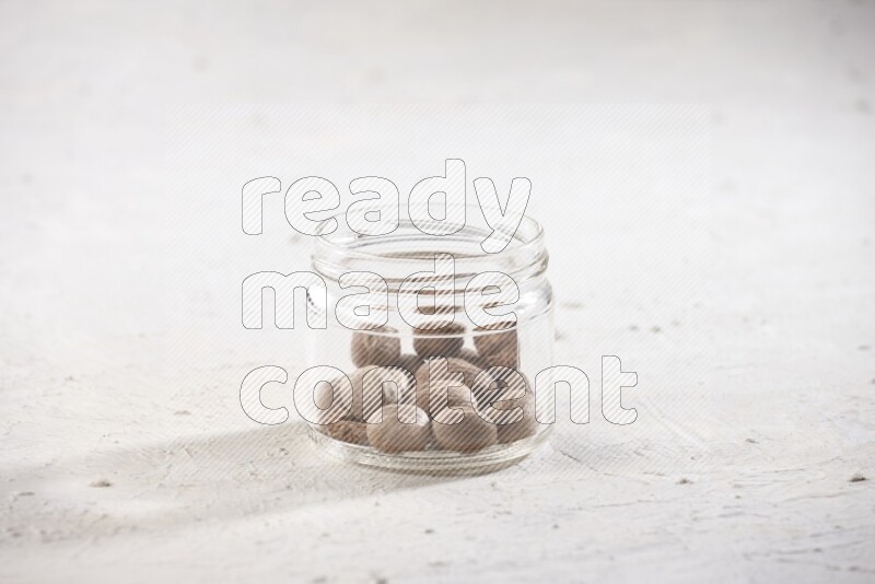 A glass jar full of whole nutmeg seeds on a white flooring
