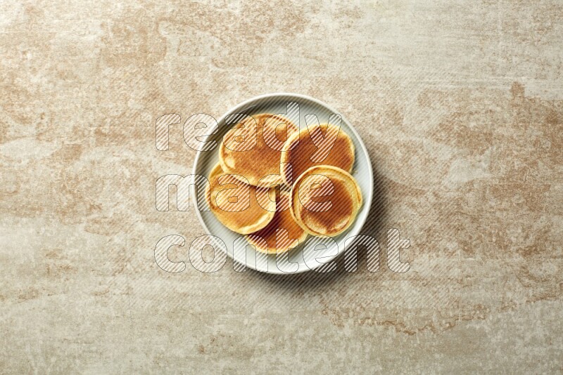 Five stacked plain mini pancakes in a blue plate on beige background