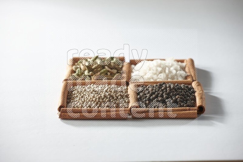 4 squares of cinnamon sticks full of cardamom, salt, white pepper and black pepper on white flooring