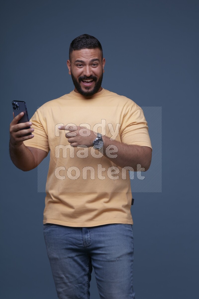 A man Pointing at a Smartphone on Blue Background wearing Orange T-shirt