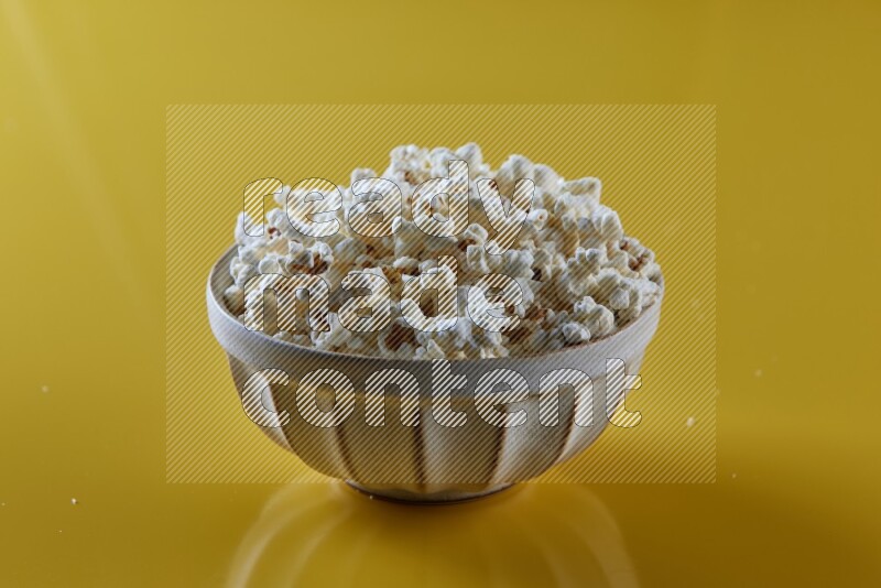 A white pottery bowl full of popcorn on a yellow background in different angles