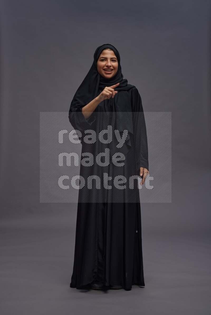 Saudi woman wearing Abaya standing interacting with the camera on gray background