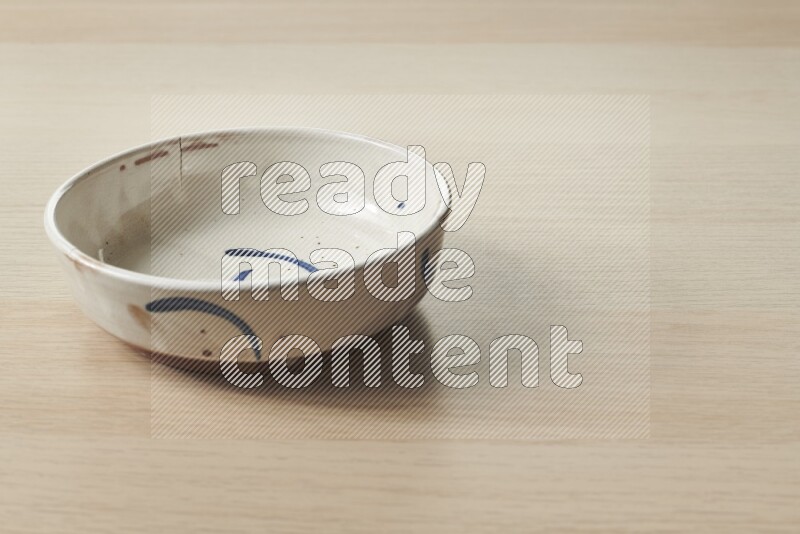 وعاء فخاري متعدد الألوان على خلفية خشبية فاتحة