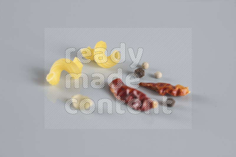 Raw pasta with different ingredients such as cherry tomatoes, garlic, onions, red chilis, black pepper, white pepper, bay laurel leaves, rosemary, cardamom and mushrooms on light blue background