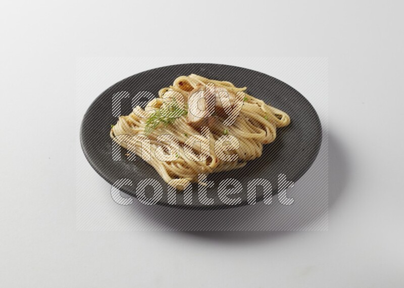 spaghetti pasta with white sauce on a black plate on a white background
