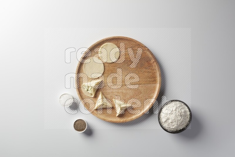 two closed sambosas and one open sambosa filled with cheese while flour, salt, and black pepper aside in a wooden dish on a white background