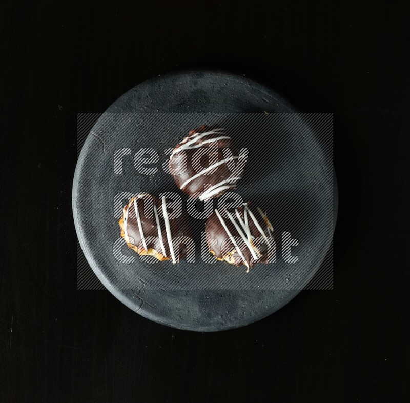 Assorted desserts in a black pottery plate on black background