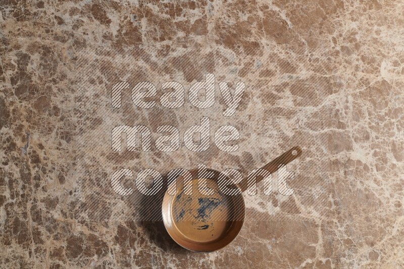 A small copper pan on beige marble background