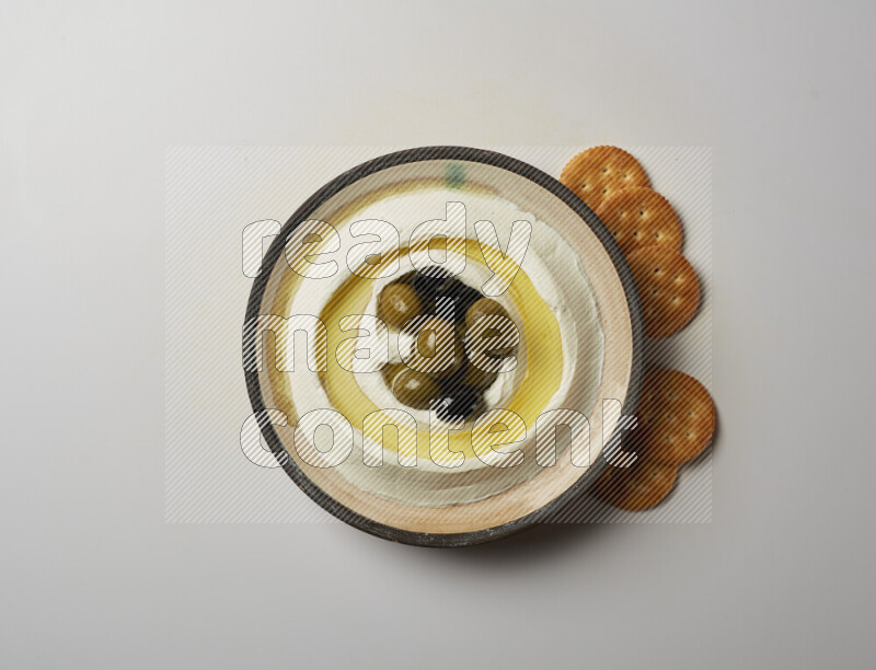 Lebnah garnished with whole black olives in a pottery plate on a white background