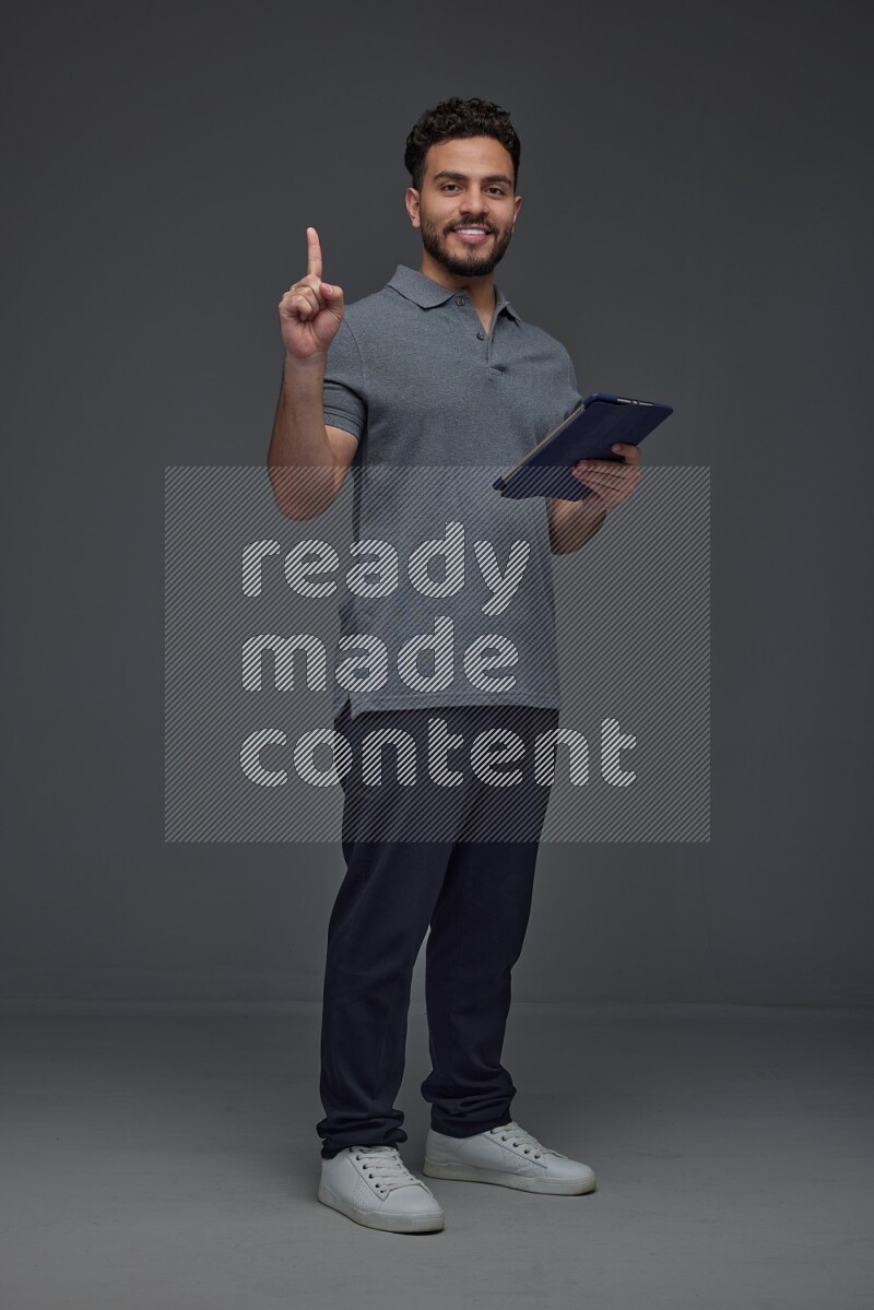 A man wearing casual standing and using his tablet and making multi hand gestures different angles eye level on a gray background