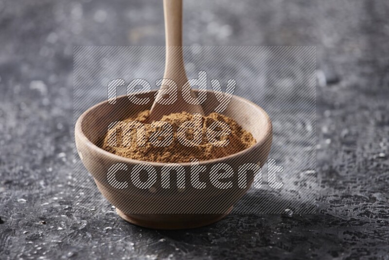 Wooden bowl full of cinnamon powder with a wooden spoon on a textured black background in different angles