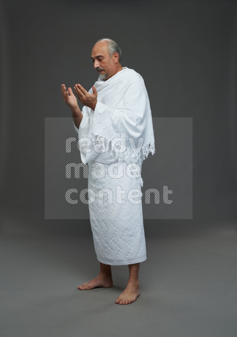 A man wearing Ehram Standing dua'a on gray background