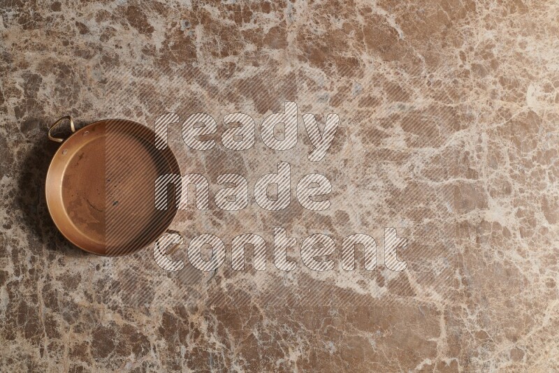 A small copper pan on beige marble background