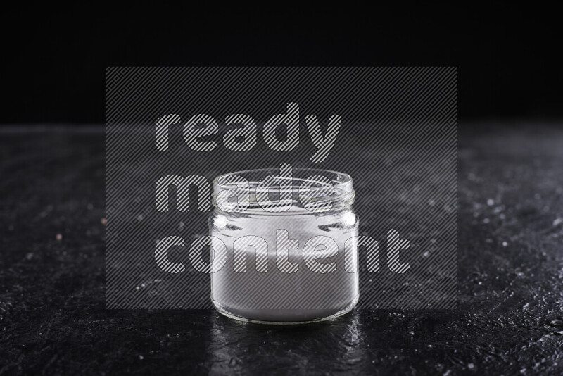 A glass jar full of fine table salt on black background
