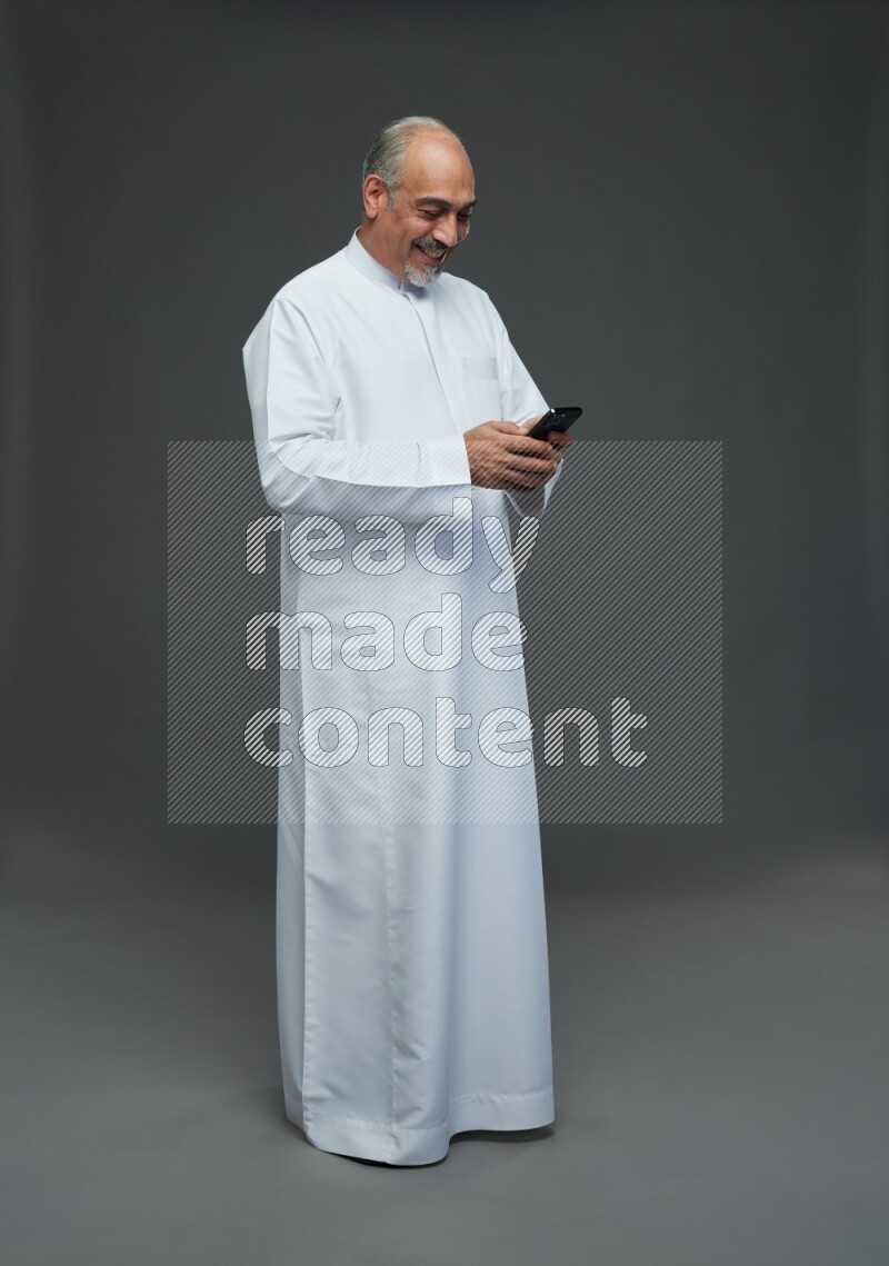 Saudi man without shomag Standing texting on phone on gray background