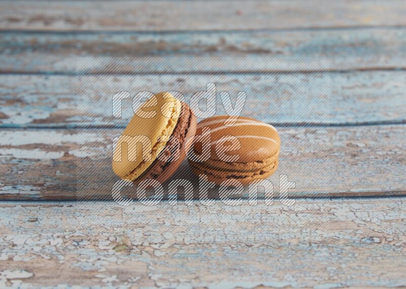 45º Shot of of two assorted Brown Irish Cream, and Yellow, and Brown Chai Latte macarons  on light blue background