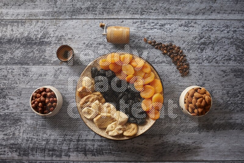 Dried fruits in a pottery plate with nuts and coffee in a dark setup