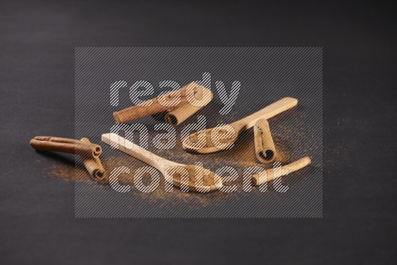 Cinnamon powder in two wooden spoons with cinnamon sticks on black background
