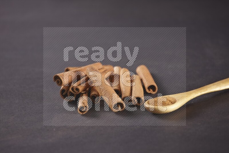 Cinnamon sticks stacked beside a wooden spoon full of cinnamon powder on black background