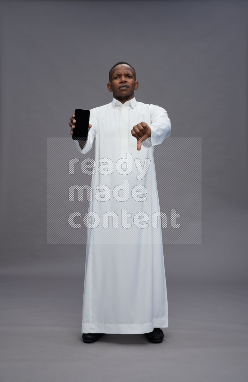 Saudi man wearing thob standing showing phone to camera on gray background